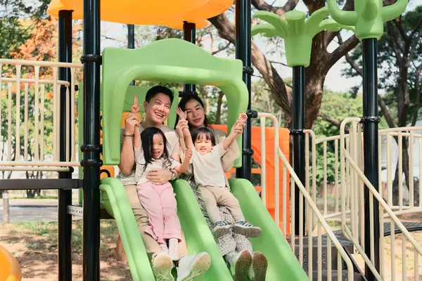 Dört kişilik mutlu bir aile oyun alanında birlikte kayıyor..