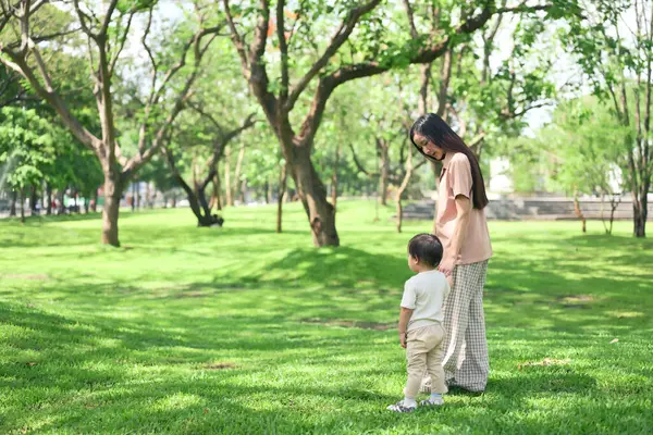 Güneşli bir günde huzur dolu yeşil bir parkta el ele tutuşan anne ve bebek..
