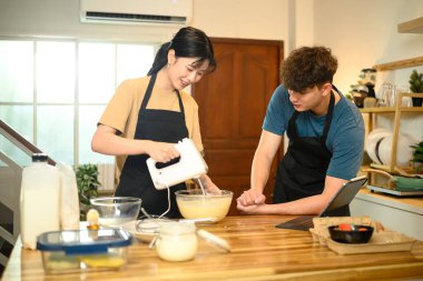 Gülümseyen çift birlikte krep hamuru yapıyor. Mutfakta el çırpıcı kullanıyorlar..