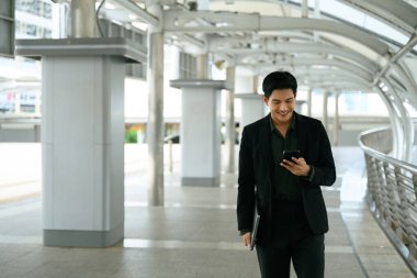 Modern şehir geçidinde yürüyen ve akıllı telefon kullanan kendine güvenen bir yönetici..