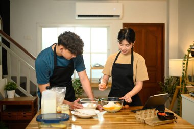 Genç çift birlikte krep hamuru hazırlarken una yumurta kırıyor..