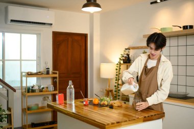 Önlüklü genç adam mutfakta kahvaltı hazırlarken süt koyuyor..