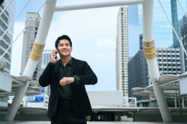 Kendine güvenen işadamı, akıllı saati kontrol ediyor, modern bir şehirde duruyor..