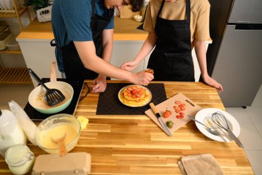 Sevgi dolu genç bir çift ev yapımı krepleri birlikte dilimlenmiş çilekle süslüyorlar..