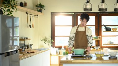 Mutfakta yemek hazırlarken gülümseyen genç bir adam, ocağın başında duruyor..
