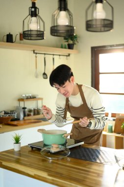 Mutfakta yemek hazırlarken gülümseyen genç bir adam, ocağın başında duruyor..