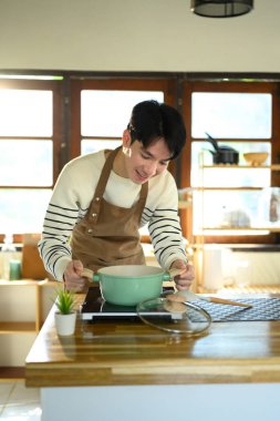 Mutfakta yemek hazırlarken gülümseyen genç bir adam, ocağın başında duruyor..
