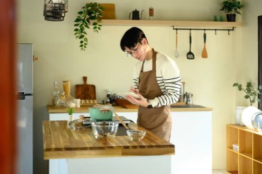 Önlüklü genç adam mutfakta yemek hazırlarken not alıyor..