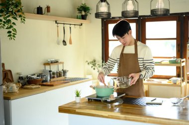 Genç adam mutfakta yemek pişirirken tencerede yemek pişiriyor..