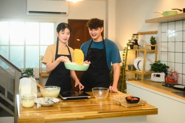 Neşeli genç çift mutfakta krep çevirirken birlikte eğleniyor..