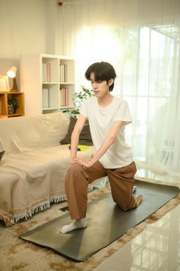 Gülümseyen Asyalı genç adam oturma odasındaki paspasla yoga yapıyor..