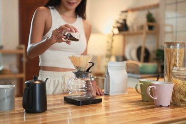 Genç bir kadın sıcak bir ev mutfağında cam damlatıcı kullanarak kahvenin üzerine dökme hazırlıyor..