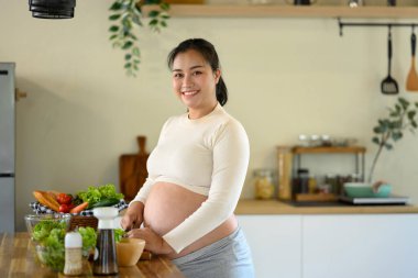 Mutlu hamile kadın mutfak tezgahında durup sağlıklı bir yemek hazırlıyor..