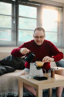 Mutlu, yaşlı bir adam evde cam damlatıcı ve su ısıtıcısıyla dikkatli bir şekilde kahve yapıyor..