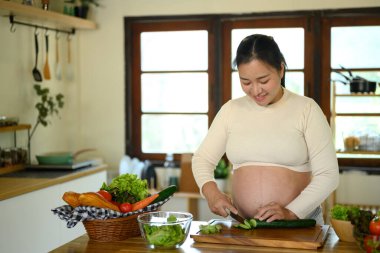 Mutlu hamile kadın mutfak tezgahında durup sağlıklı bir yemek hazırlıyor..