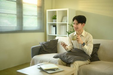 Gülümseyen adam oturma odasında otururken akıllı telefondan mesajları ya da uyarıları kontrol eder.