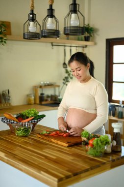 Mutlu hamile kadın mutfak tezgahında durup sağlıklı bir yemek hazırlıyor..
