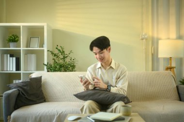 Gülümseyen adam oturma odasında otururken akıllı telefondan mesajları ya da uyarıları kontrol eder.