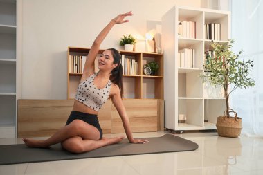 Zarif yoga pratiği yapan güzel Asyalı kadın huzurlu bir oturma odasında esniyor..