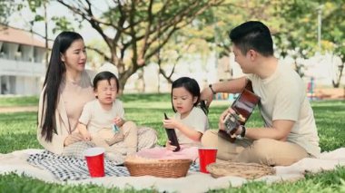 Mutlu bir aile parkta battaniyede pikniğin tadını çıkarıyor..