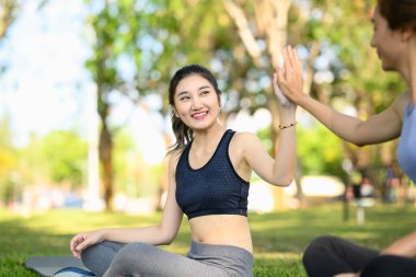 İki atletik kadın yeşil bir parkta spor yaptıktan sonra keyifli bir beşliği paylaşıyor...