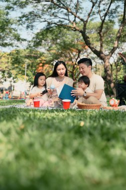 Ebeveynler dışarıda battaniyenin üzerinde dinlenirken küçük çocuklarına kitap okurlar..