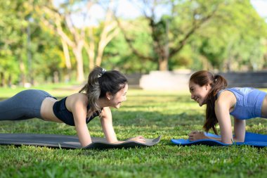 Mutlu bayan arkadaşlar parktaki yoga minderleri üzerinde tahta egzersizleri yapıyorlar..