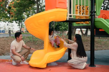 Neşeli küçük kız, sevgi dolu anne ve babasının desteğiyle kaymaktan zevk alıyor..