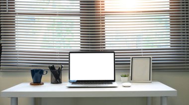 Geniş pencere perdelerinin önünde boş laptop ekranı olan çağdaş ofis masası.