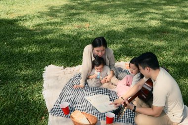 Ebeveynler dışarıda battaniyenin üzerinde dinlenirken küçük çocuklarına kitap okurlar..