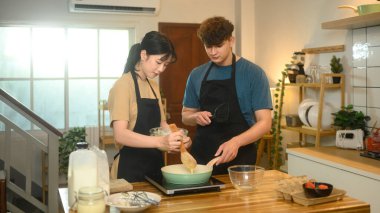 Önlük giyen mutlu çift modern mutfakta kahvaltı hazırlıyor..