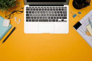 Sarı arka planda dizüstü bilgisayarı, kırtasiyesi ve belgeleri olan modern çalışma alanı düzlüğü.