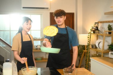 Neşeli çift krep yapıyor, ev yemekleri sırasında kahkahalarını paylaşıyorlar..