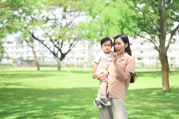 Asyalı anne ve küçük çocuğu yemyeşil bir parkta geziyorlar..