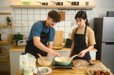 Önlük giyen mutlu çift modern mutfakta kahvaltı hazırlıyor..