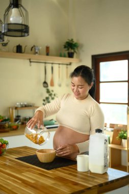 Hamile kadın sağlıklı bir kahvaltı için mısır gevreği dolduruyor..