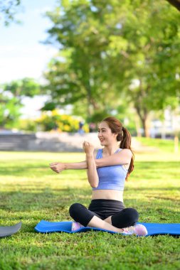 Spor kıyafetleri içinde gülümseyen kadın çimen tarlasında egzersiz yapmak için ısınıyor..