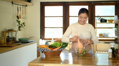 Mutlu hamile kadın evde sağlıklı bir salata hazırlıyor..