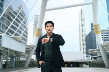 Siyah takım elbiseli kendine güvenen bir işadamı modern bir şehirde dikilirken ukalalığına bakıyor..