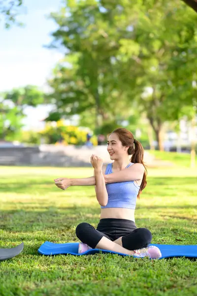 Spor kıyafetleri içinde gülümseyen kadın çimen tarlasında egzersiz yapmak için ısınıyor..