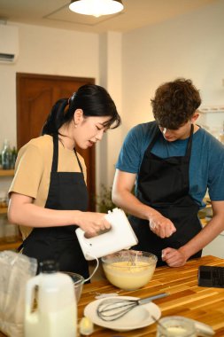 Önlüklü genç çift krep hamuru hazırlıyor ve dijital tabletteki bir tarifi takip ediyor..