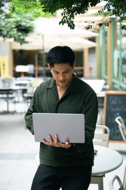 Modern bir açık hava kafesinde dizüstü bilgisayarla çalışan gülümseyen bir adam..