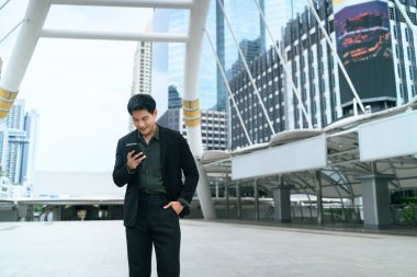 Modern bir şehir bölgesinde yürürken akıllı telefonunu kontrol eden bir iş adamı..