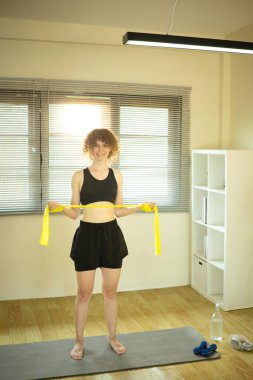 Parlak oturma odasında direniş bandıyla çalışan atletik bir kadın..