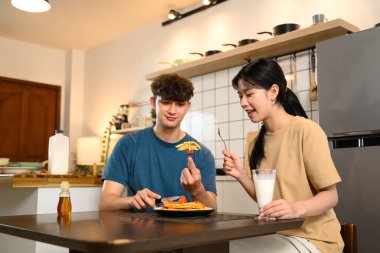 Mutlu genç çift yemek masasında birlikte ev yapımı krep yiyor..