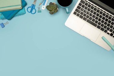 Dizüstü bilgisayarı, kırtasiyesi ve pastel mavi arka planda kahve fincanı olan modern çalışma alanının üst görüntüsü.