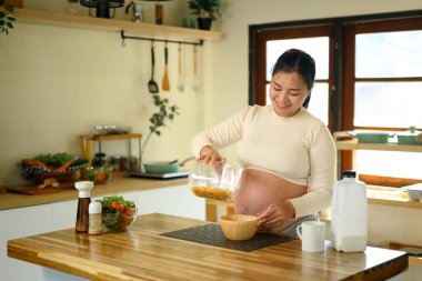 Neşeli hamile kadın mutfakta basit ve sağlıklı bir kahvaltı hazırlıyor..