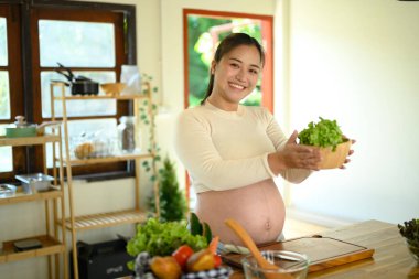 Mutlu hamile kadın evde taze malzemelerle besleyici bir yemek hazırlıyor..