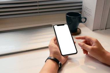 Masada boş ekranlı ve doğal ışık alan akıllı telefonu tutan elleri kapat.