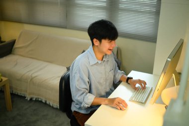 Ev bilgisayarında çalışan gülümseyen Asyalı adam..